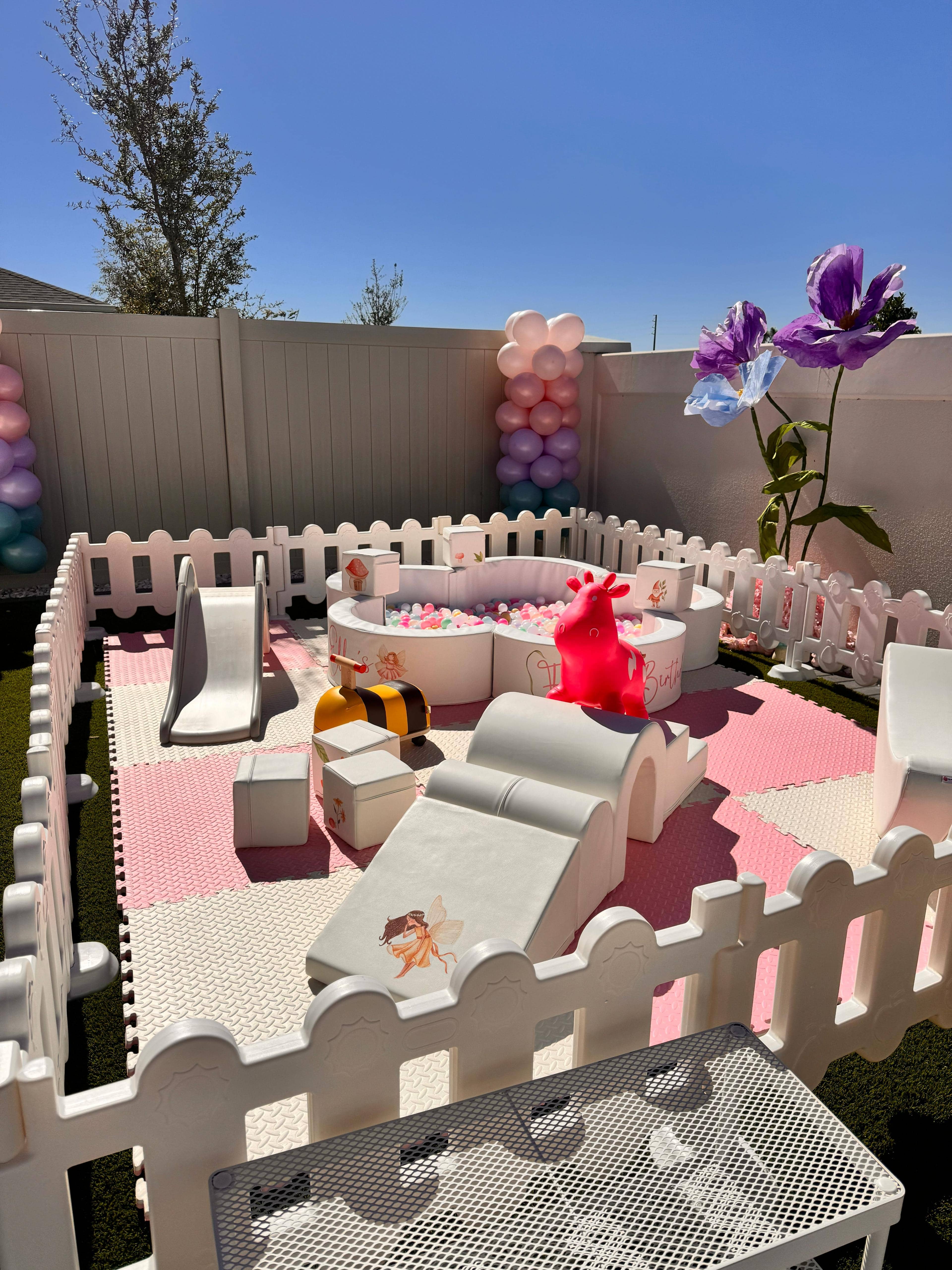 Blush and Bloom Deluxe outdoor party setup — fenced pink soft play with ball pit and peach floral bounce house for toddler birthday parties