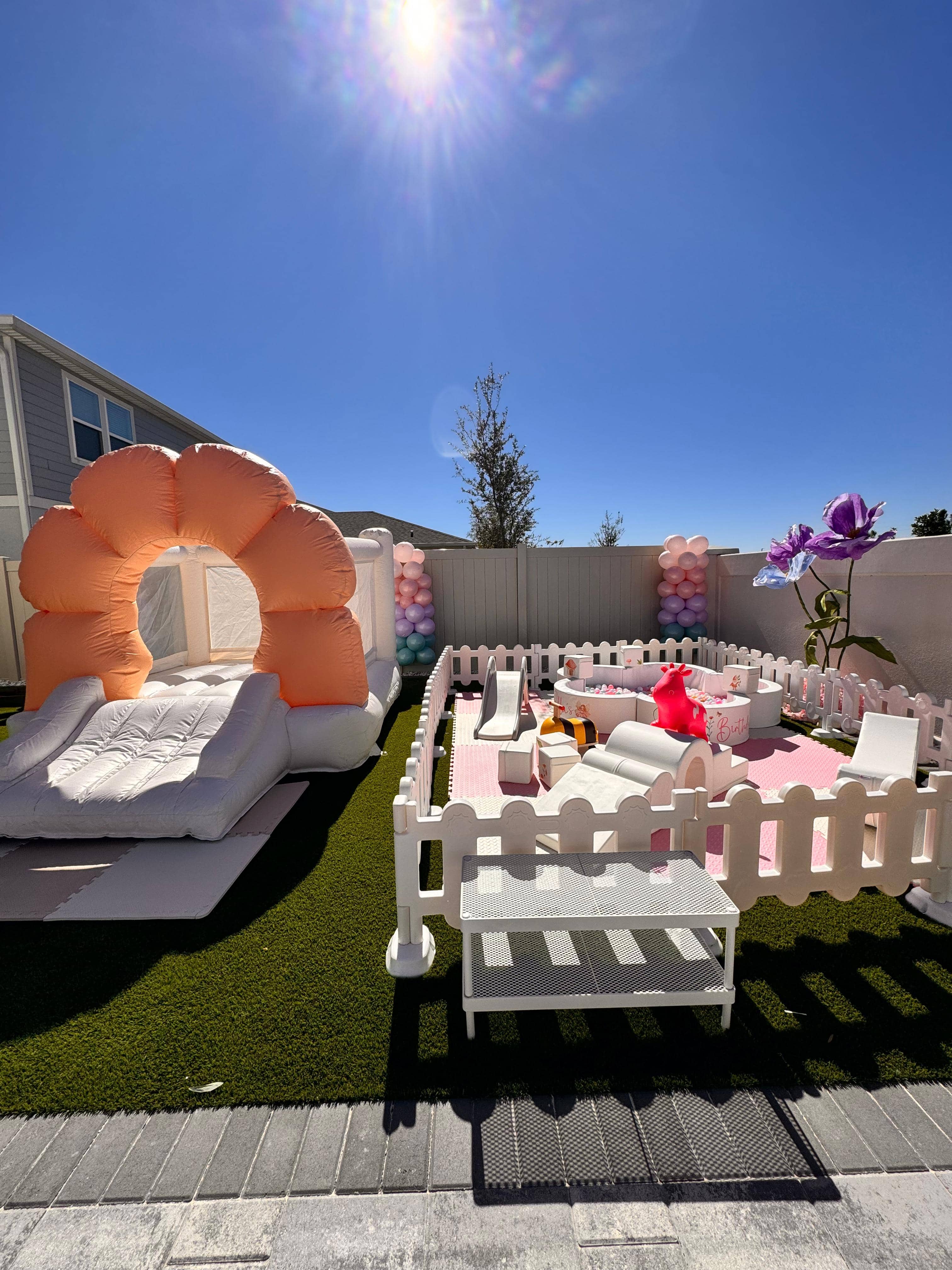 Blush and Bloom Deluxe soft play rental with pink fenced play area and peach floral bounce house side by side in a backyard