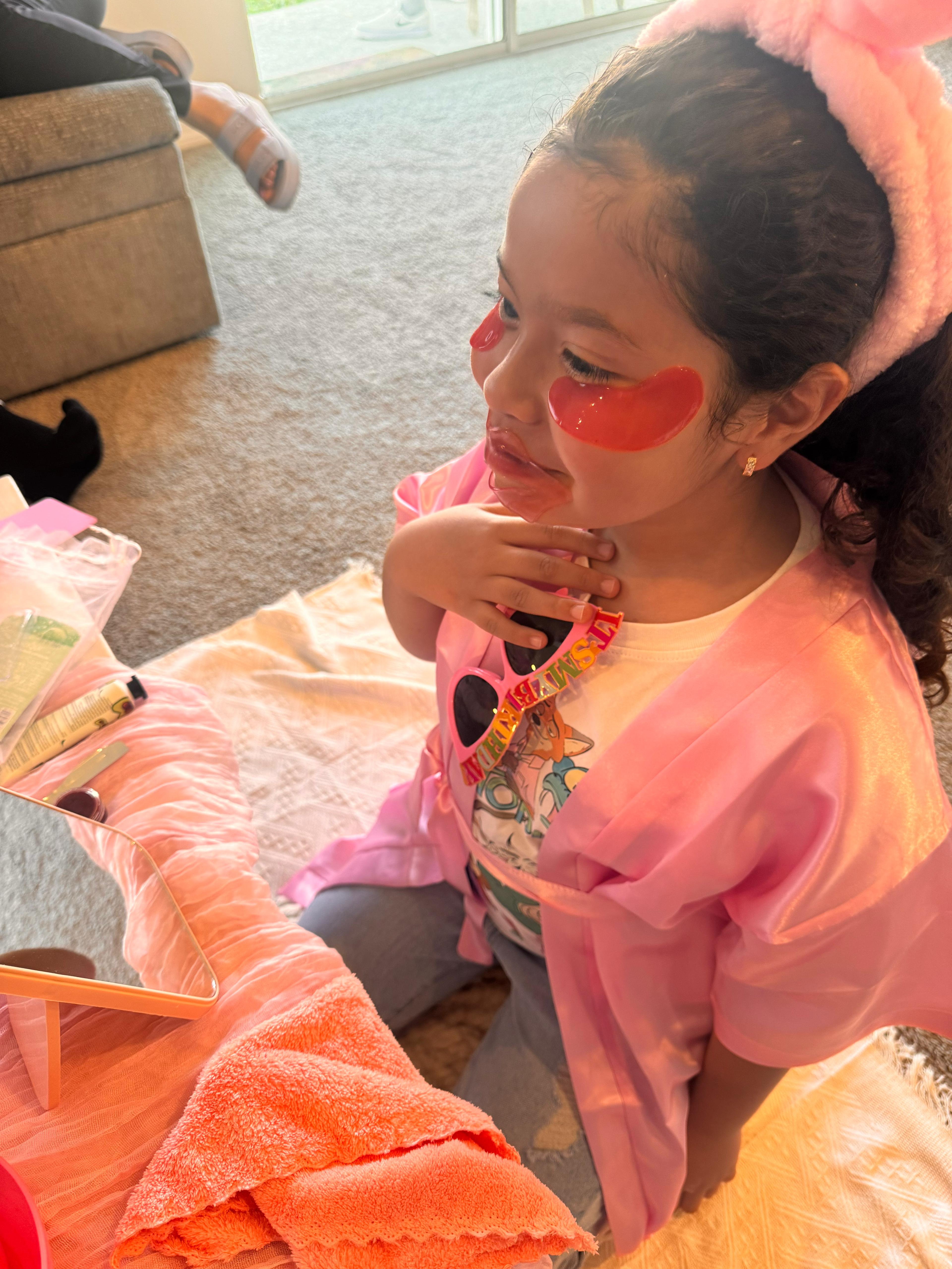 Young girl in pink spa robe applying under-eye gel patches during a Sparkle Spa kids birthday party